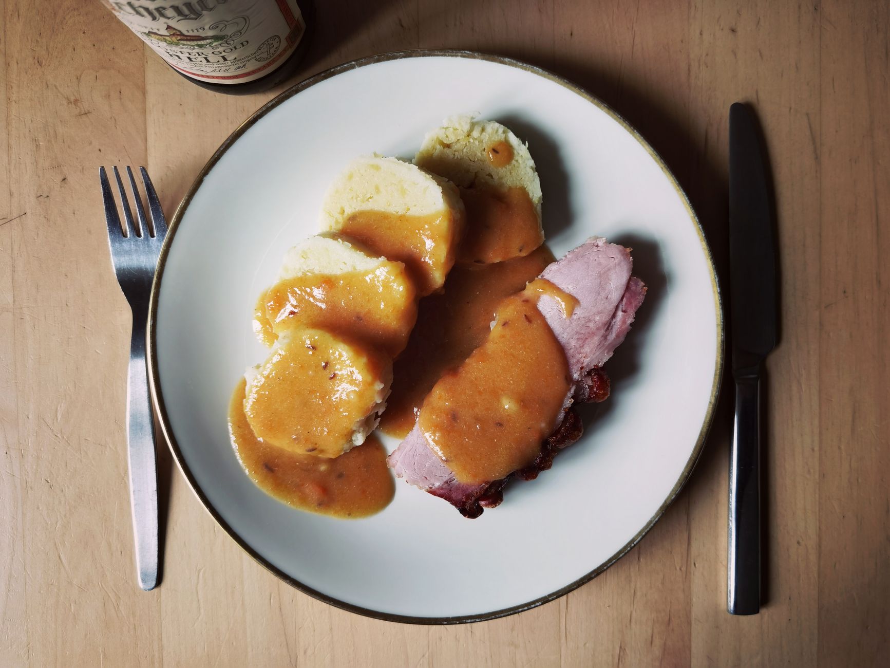 Deftiger Braten mit Knödeln und Sauce auf Holztisch